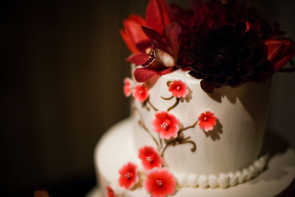 Wedding cake floral details - White tiered round wedding cake with coral floral decoration and dark red and coral topper - wedding photo by Michael Norwood Photography